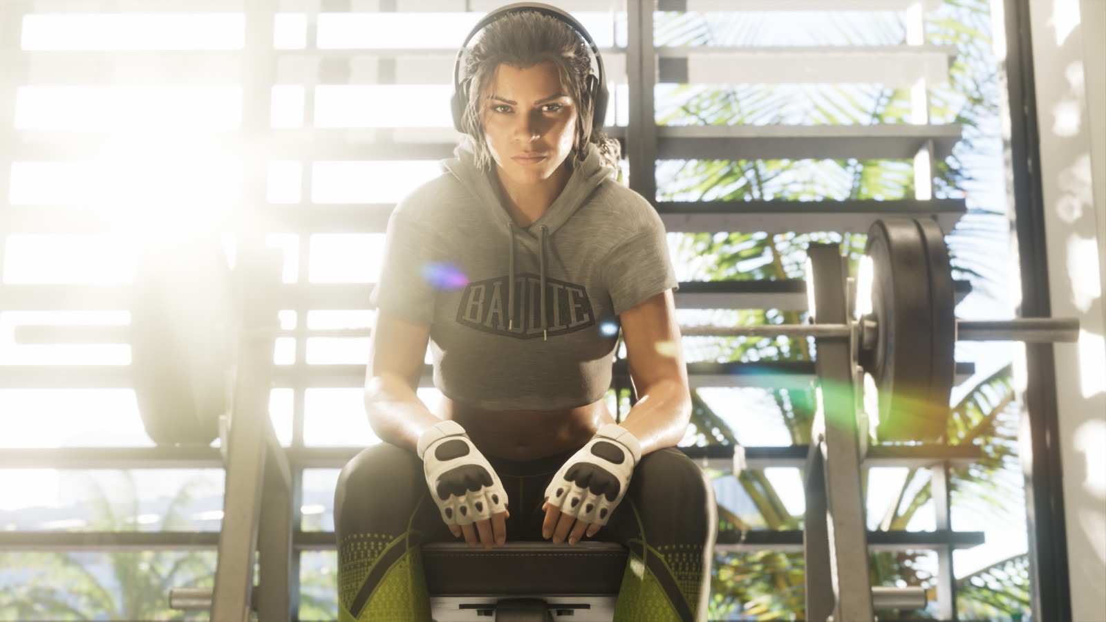 Lucia sitting on a weight bench in a gym, wearing headphones and lifting gloves